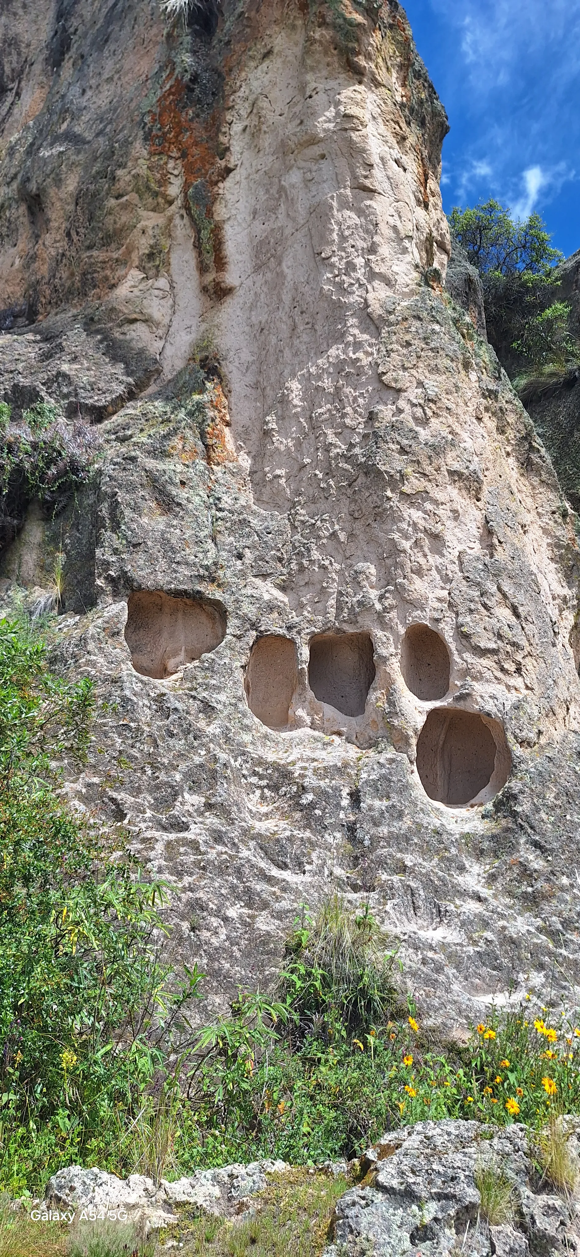 Visitante frente a las ventanillas del Complejo Arqueológico de Allpas viendo de cerca los nichos funerarios tallados en la roca